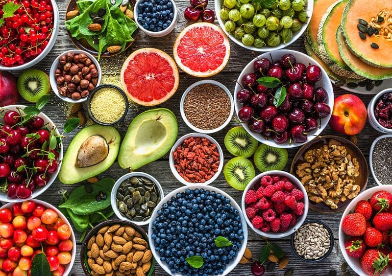 Bowls of fresh fruit, berries, nuts and seeds on a wooden table