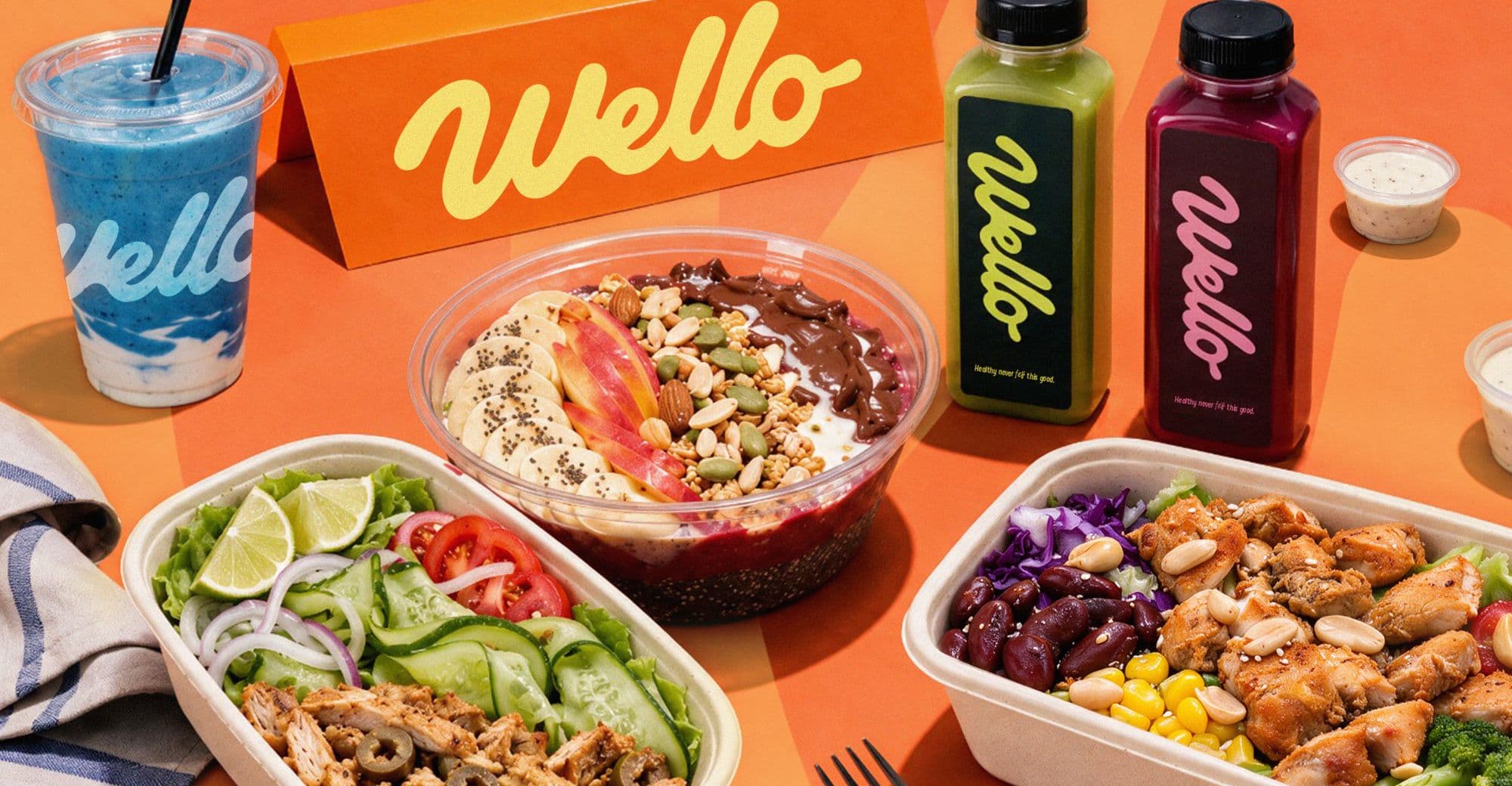 Wello juices, smoothie, acai bowl and salad bowls on an orange table